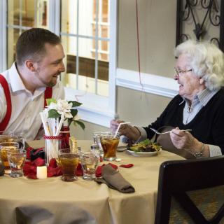 A man and an elderly woman enjoying a conversation over a meal at a restaurant.