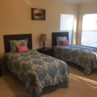 A cozy bedroom with two twin beds adorned with patterned bedspreads, a shared bedside table, and a lamp by the window.
