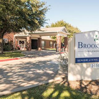 Entrance of a building with a sign and surrounding trees on a sunny day.