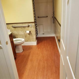 A bathroom featuring a toilet, shower with grab bars, and wooden flooring.