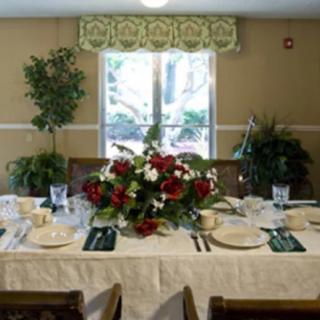 A dining table set with a floral centerpiece, surrounded by elegant place settings and indoor plants near a window.