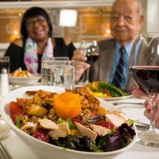 A couple enjoying a meal with wine at a restaurant, featuring a diverse salad in the foreground.