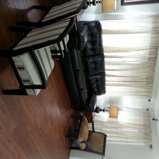 A cozy living room with a black leather sofa, striped chairs, and elegant lighting.