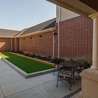 A cozy courtyard with brick walls, featuring a small patio set and an artificial grass area.