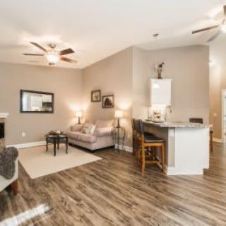 A modern open-concept living room with hardwood floors and neutral decor, featuring cozy seating and a ceiling fan.