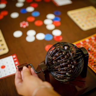 A hand turning the handle of a bingo cage, with cards and chips on the table.