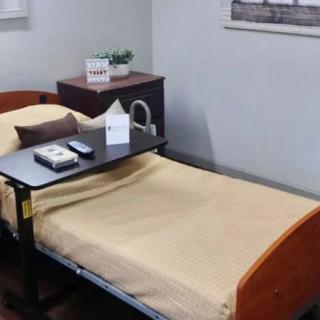 A simple medical room with a hospital bed and an over-bed table.
