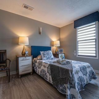 A cozy bedroom with modern decor, featuring a single bed, dual nightstands with lamps, and stylish window blinds.