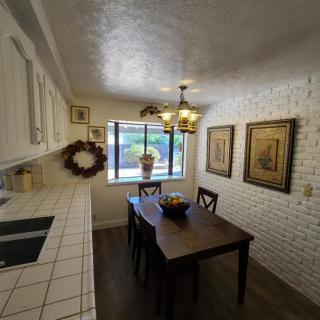 A cozy dining area with a wooden table and chairs, decorated with artwork on white brick walls and illuminated by a chandelier.