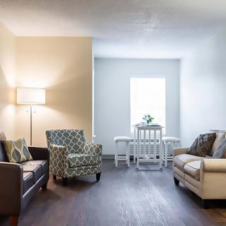 A cozy living room with sofas, a patterned chair, a lamp, and a small dining table by the window.