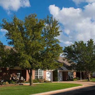 A quiet suburban neighborhood with brick houses and lush green lawns under a partly cloudy sky.