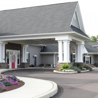 The image shows the entrance of a modern building with landscaped surroundings and prominent columns.