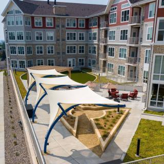 A modern apartment complex with an outdoor area featuring shade structures and greenery.