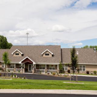 A suburban residential building with a gabled roof and surrounding greenery under a cloudy sky.