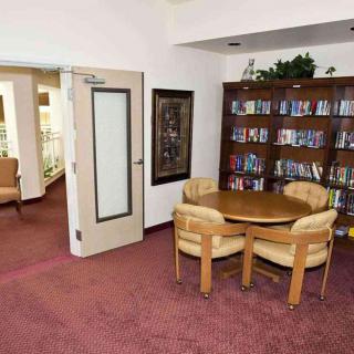 A cozy reading area in a library with bookshelves, a round table, and chairs on a carpeted floor.