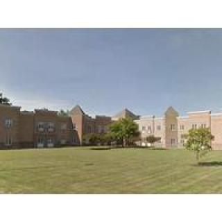 A large brick building with a well-maintained lawn and trees under a clear sky.