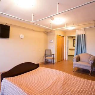 A clean and spacious hospital room with a bed, TV, and comfortable seating.