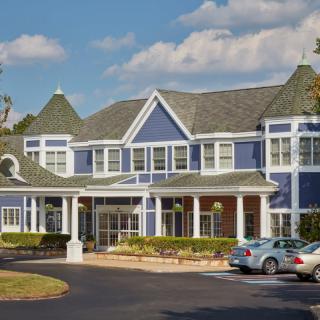 A two-story blue residential building with a driveway and parked cars.
