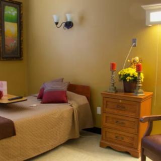 A cozy bedroom with a neatly made bed, a wooden dresser, and decorative elements such as flowers and a painting on the wall.