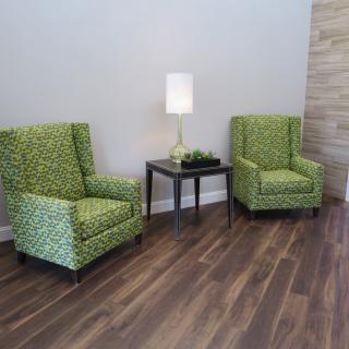 A cozy living space featuring two green patterned chairs, a small black table, and a modern lamp on a wooden floor.
