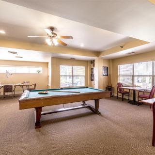 A spacious game room with a pool table and seating area, featuring large windows and a ceiling fan.