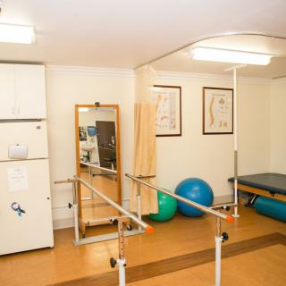 A well-equipped physical therapy and rehabilitation room featuring parallel bars, a large mirror, therapy balls, and other exercise equipment.