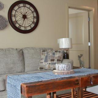 A cozy living room with a sofa, decorative wall clock, and a table with a lamp.