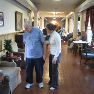 An elderly person receiving assistance in a nursing home hallway.