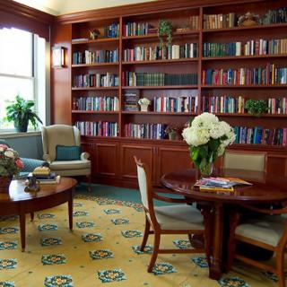 A cozy library and reading area with bookshelves, comfortable seating, and floral arrangements.