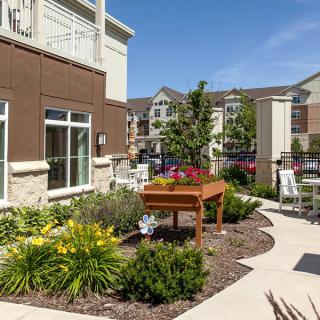 A well-maintained garden area outside a modern apartment building with lush greenery and seating.
