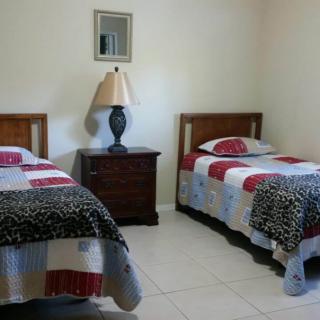 A simple bedroom featuring two twin beds with colorful quilts, a central nightstand, and a lamp.