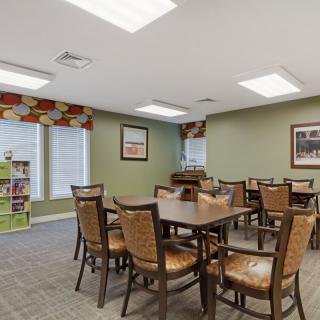 A well-lit indoor dining area with neatly arranged tables and chairs, featuring decorative windows and wall art.