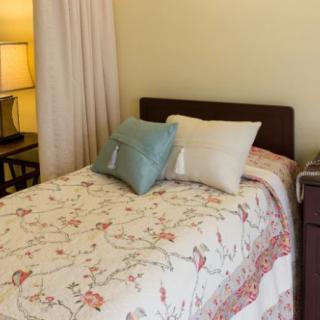 A cozy bedroom with a neatly made bed featuring decorative pillows and a floral quilt, accompanied by a warm glowing lamp.