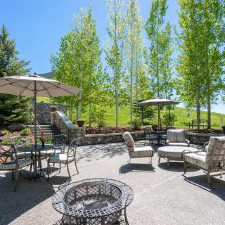 A sunny outdoor patio area with seating, tables, and umbrellas surrounded by lush trees.