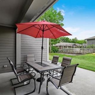 An outdoor patio setup with a table, chairs, and a red umbrella in a residential backyard.