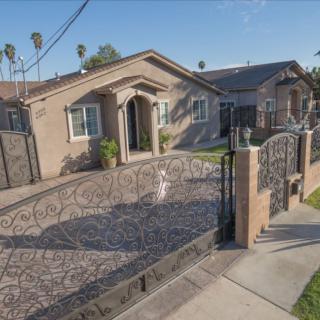 A suburban house with a gated driveway and palm trees in the background on a sunny day.