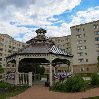 A gazebo surrounded by a tall building under a partly cloudy sky.