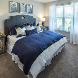 A cozy bedroom with a navy blue and white color scheme, featuring a large bed, decorative pillows, and natural light coming through the window.