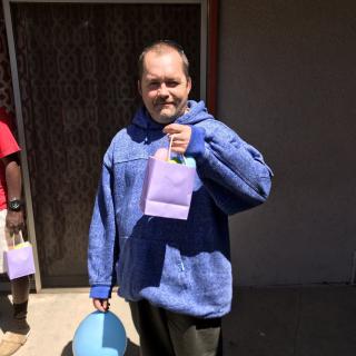 A man in a blue hoodie holding a gift bag and balloon outside.