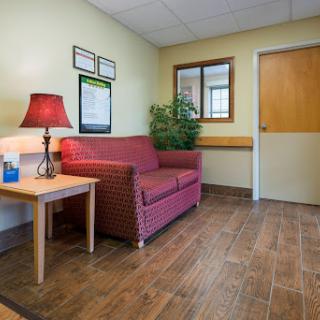 A cozy waiting area featuring a red sofa, a side table with a lamp, and decorative plants.