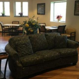 A cozy living room with a floral-patterned sofa and a dining area in the background.