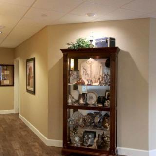 A well-lit hallway featuring a wooden display cabinet filled with decorative items and artwork on the walls.