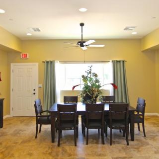 A spacious dining room with a large table, surrounded by chairs and lit by natural light streaming through the window.