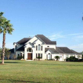 A luxury house with palm trees and a large lawn on a clear day.
