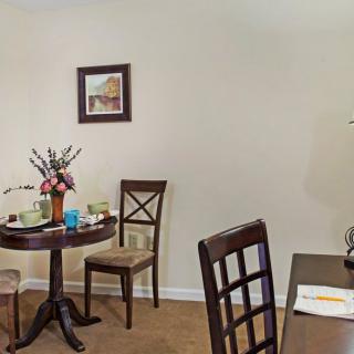 A cozy dining area with a round table and chairs, decorated with a vase of flowers and wall art.