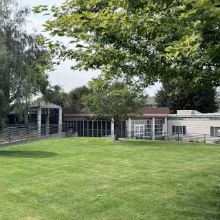A serene outdoor space featuring a landscaped lawn, modern buildings, and lush greenery.