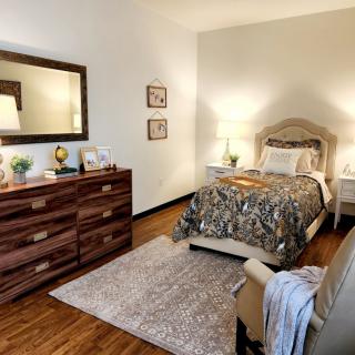 Cozy bedroom with a warm and inviting interior featuring a bed, dresser, and soft lighting.