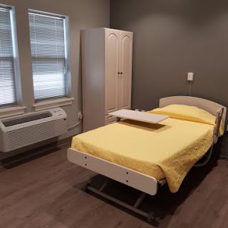 A hospital room featuring a bed with a yellow blanket and medical furniture.