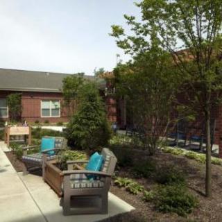 A peaceful courtyard with outdoor seating and lush greenery next to a brick building.