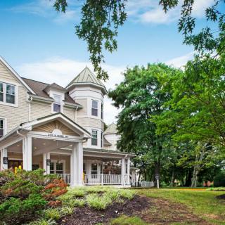 A charming residential house with a wraparound porch and lush greenery.